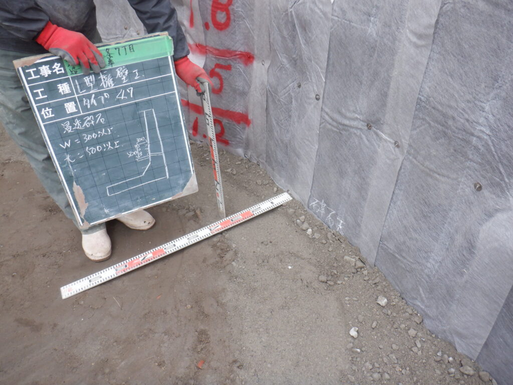 擁壁背面の止水コンクリート上に施工した浸透砕石の幅と高さを確認している状態
